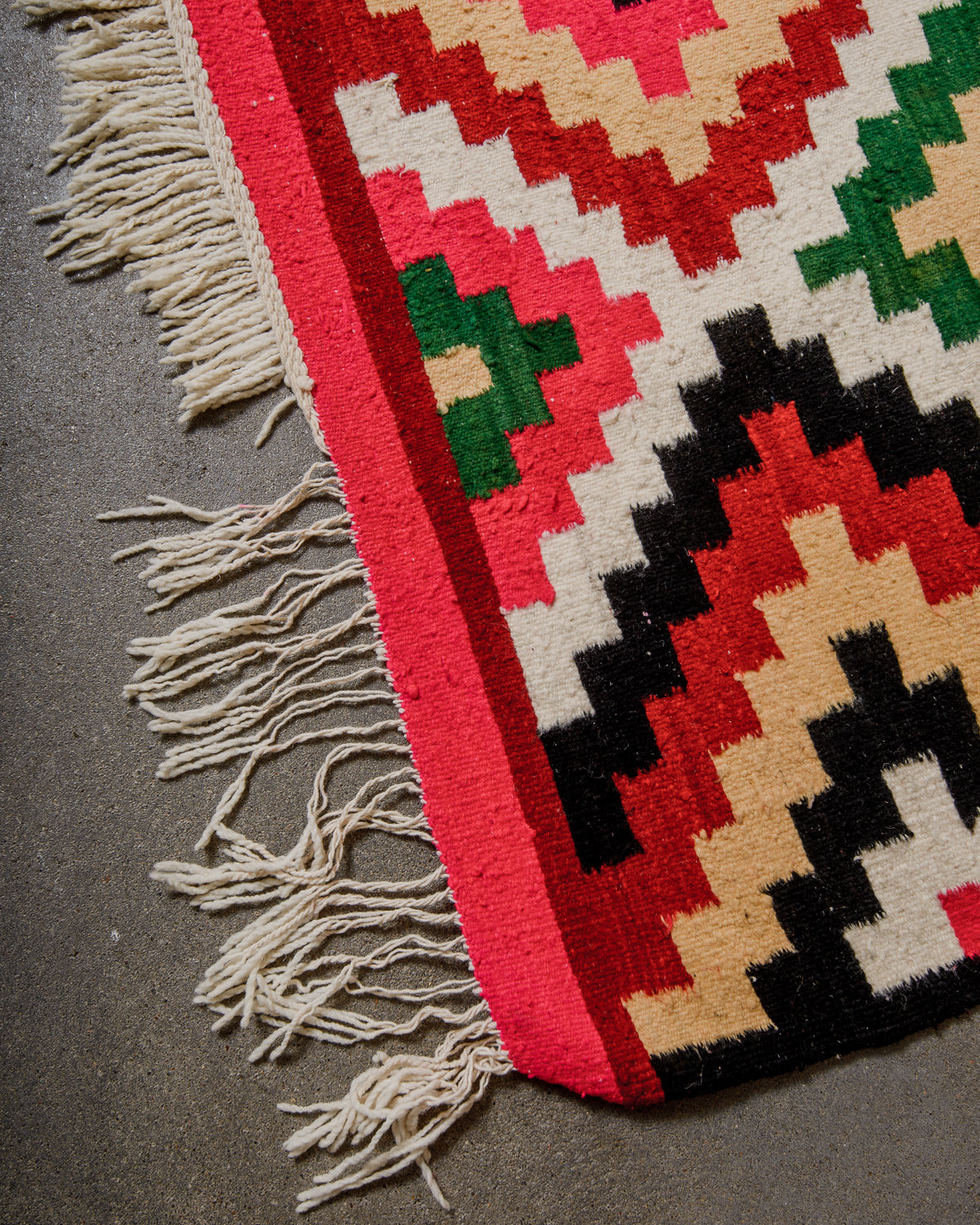 Close-up of a colorful geometric-patterned rug with fringes on a gray surface