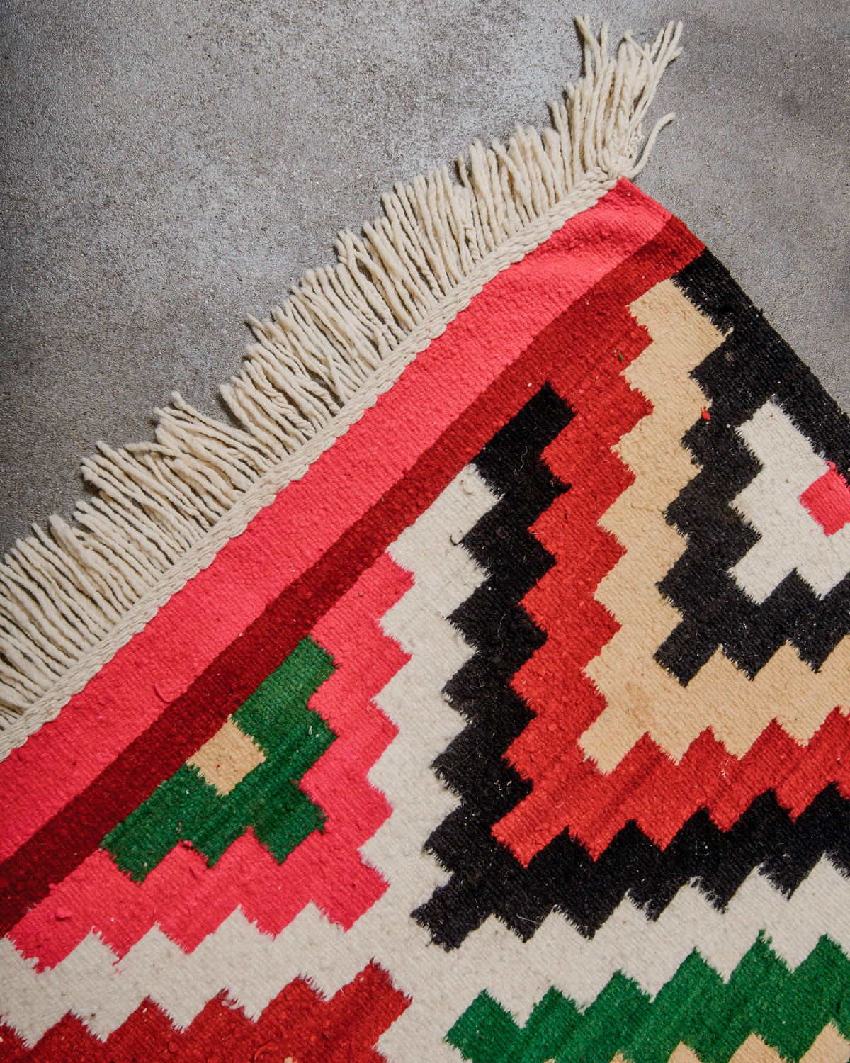 Close-up of a colorful geometric-patterned rug with fringes on a gray surface