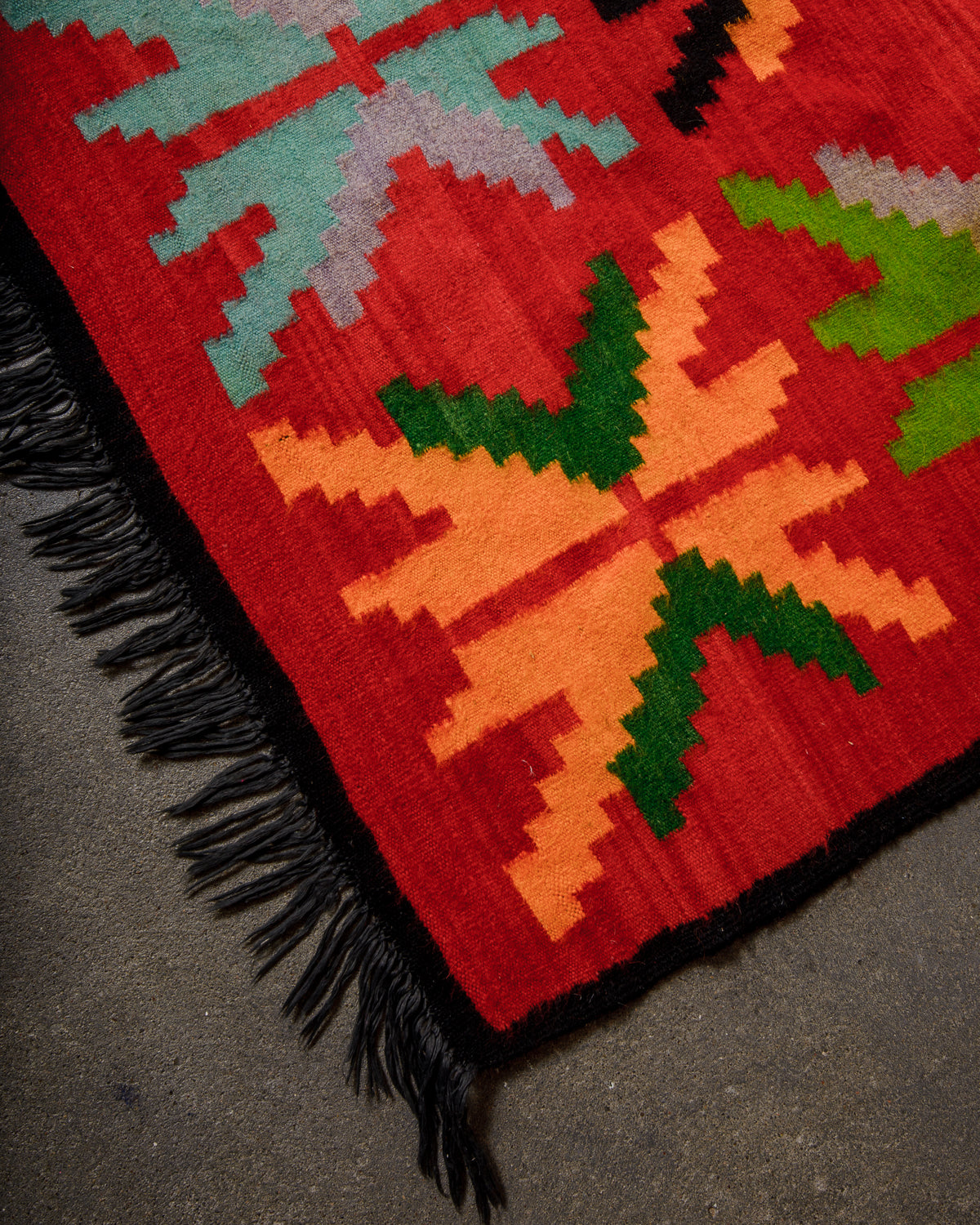 Close-up of a colorful geometric-patterned rug with fringes on a dark surface