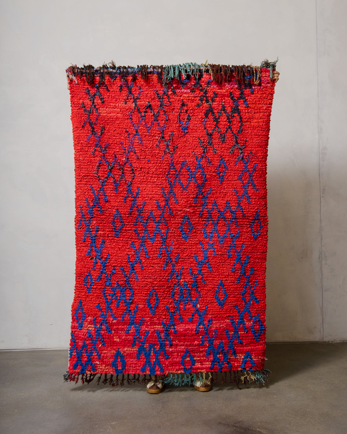 Red and blue patterned woven art piece against a gray wall.