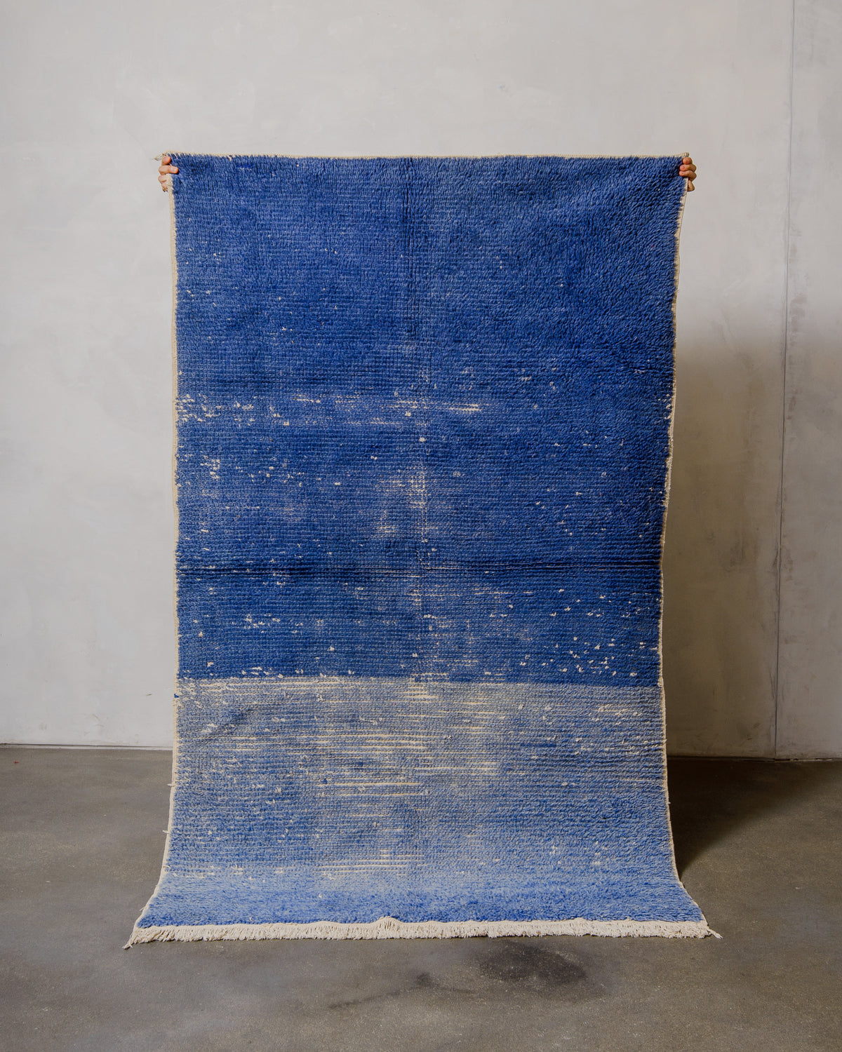 Blue rug with gradient pattern on a gray floor against a gray wall