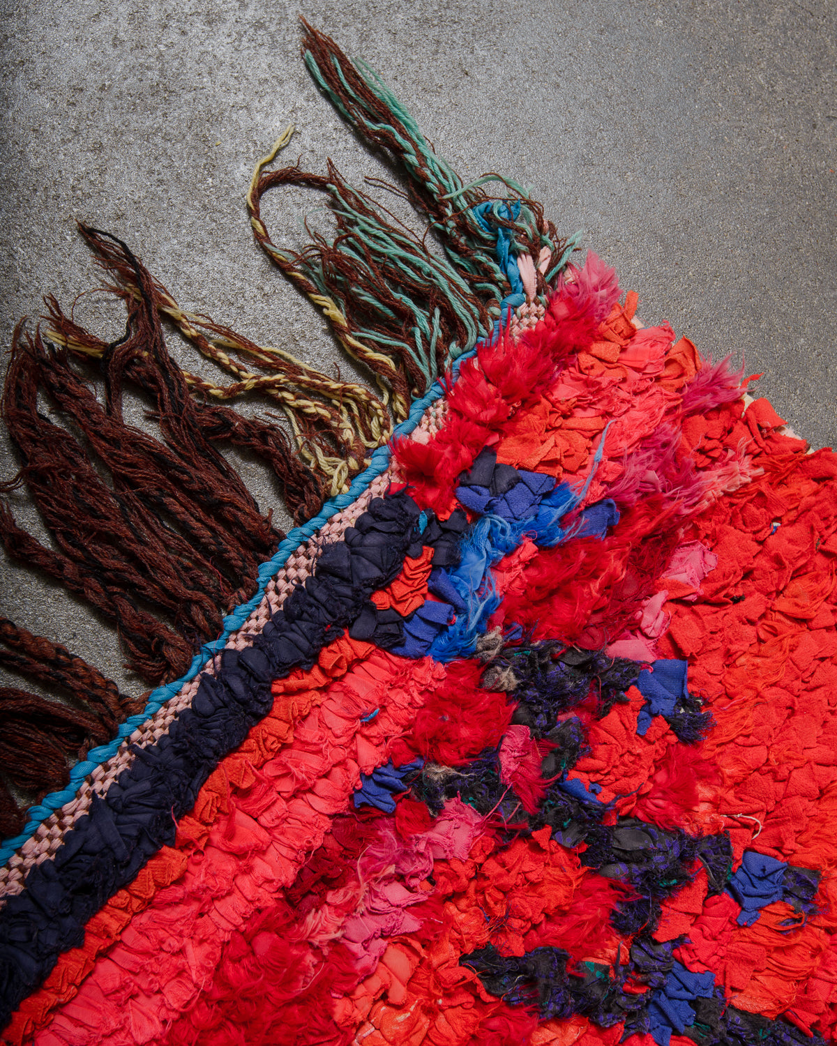 Close-up of a colorful woven rug with tassels on a gray surface