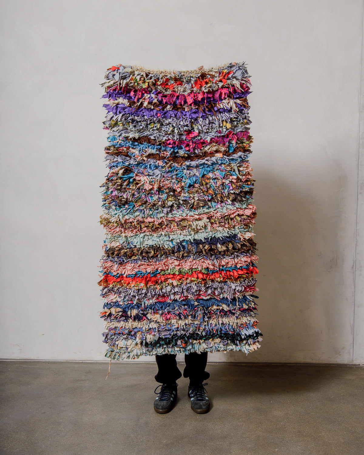 Multicoloured woven textile rug against a plain wall.