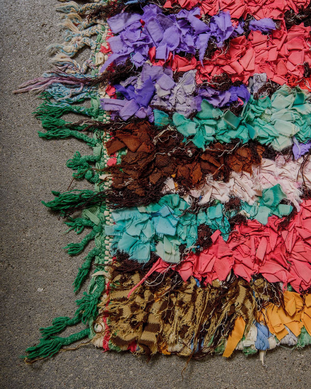 Multicoloured textured rug with fringe on a concrete floor.