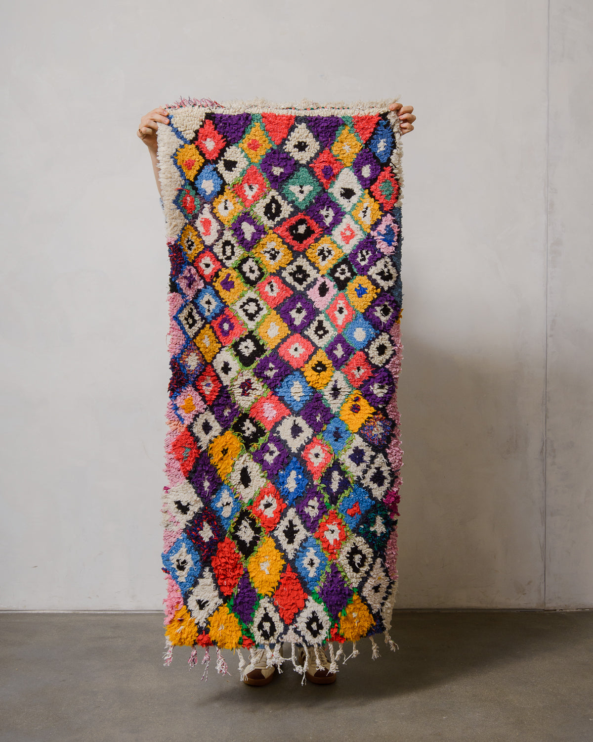 Multicolored patterned rug held by a person against a plain background