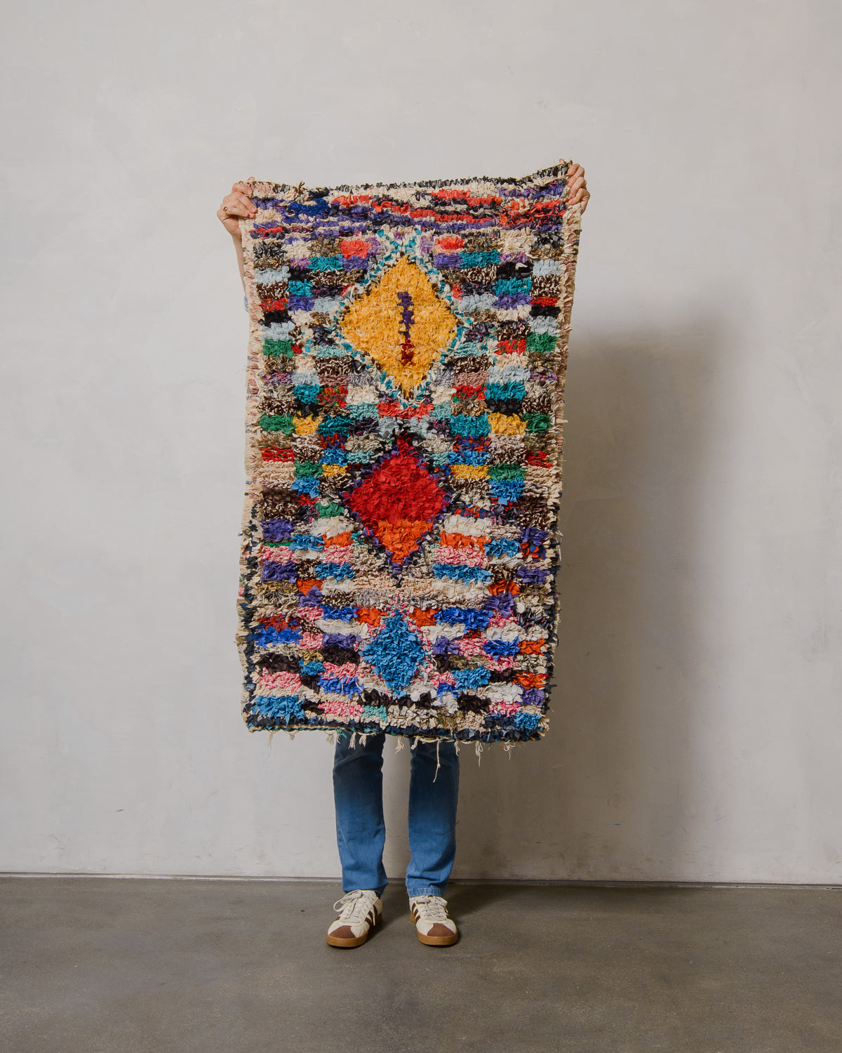 Person holding a colorful patterned rug against a plain wall
