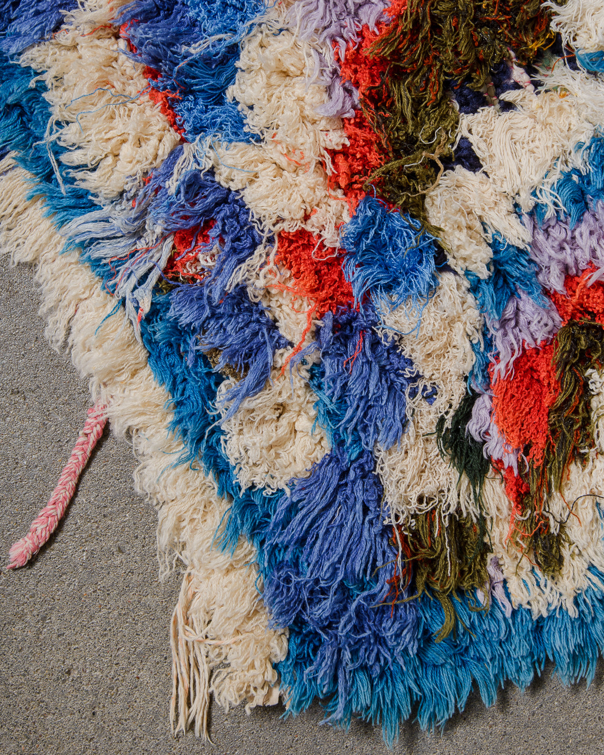 Multicolored textured fabric with blue, red, and beige tones on a gray surface.