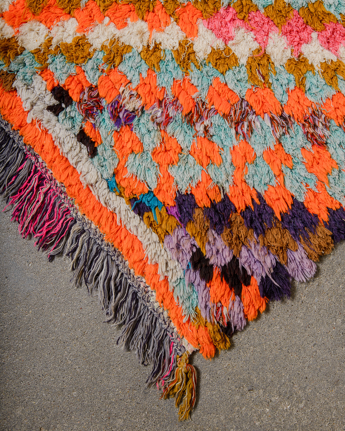 Colorful boucherouite rug with fringe on a gray surface