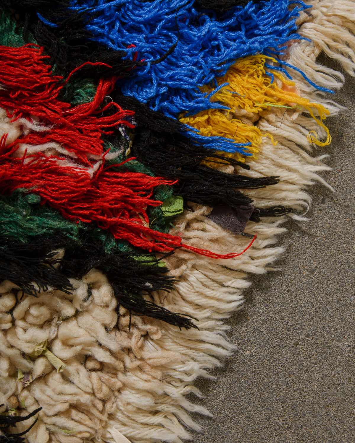 Close-up of a colorful woven rug with red, blue, yellow and green and an edge of sheep's wool.