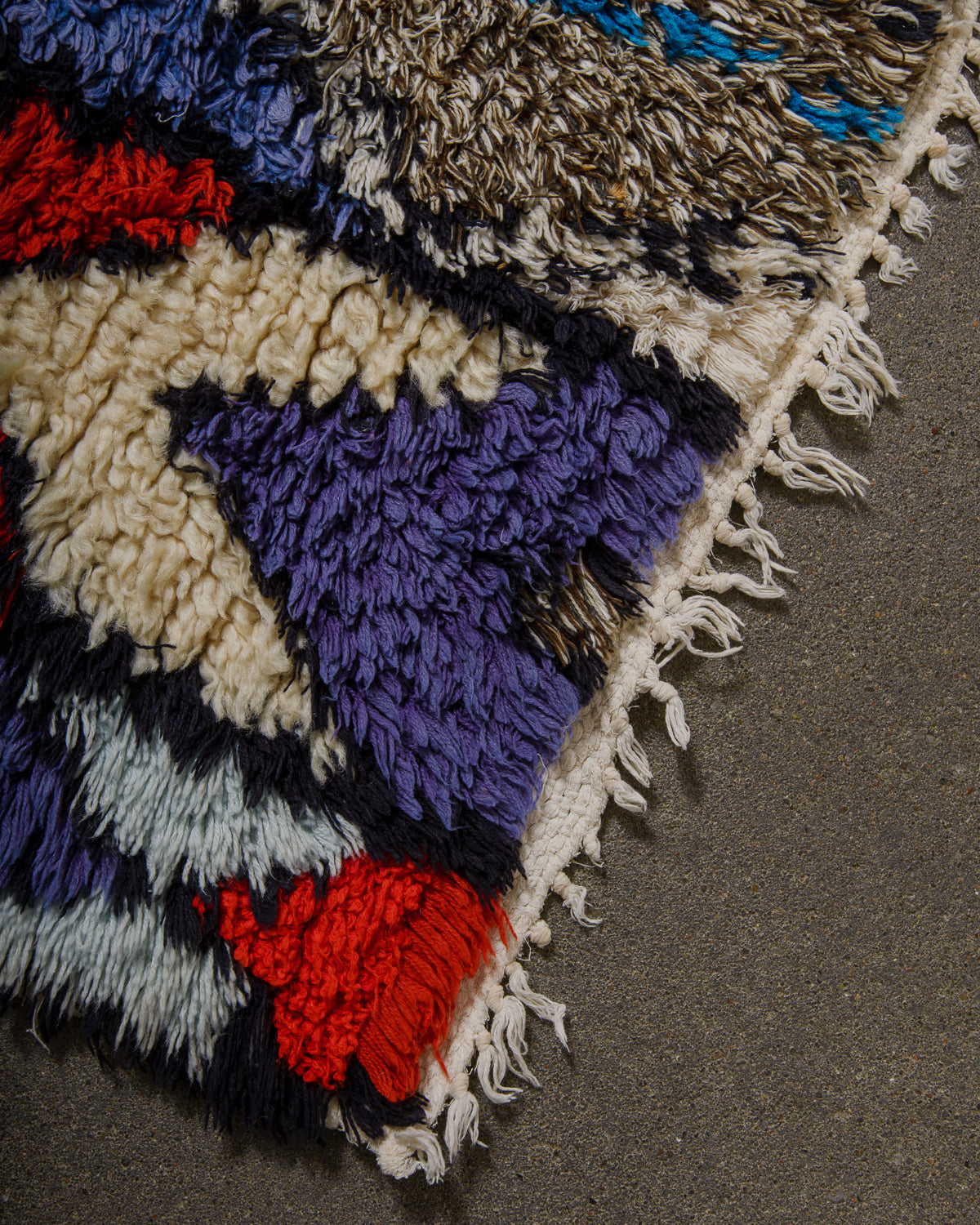 Close-up of a colorful woven rug with fringe on a gray surface