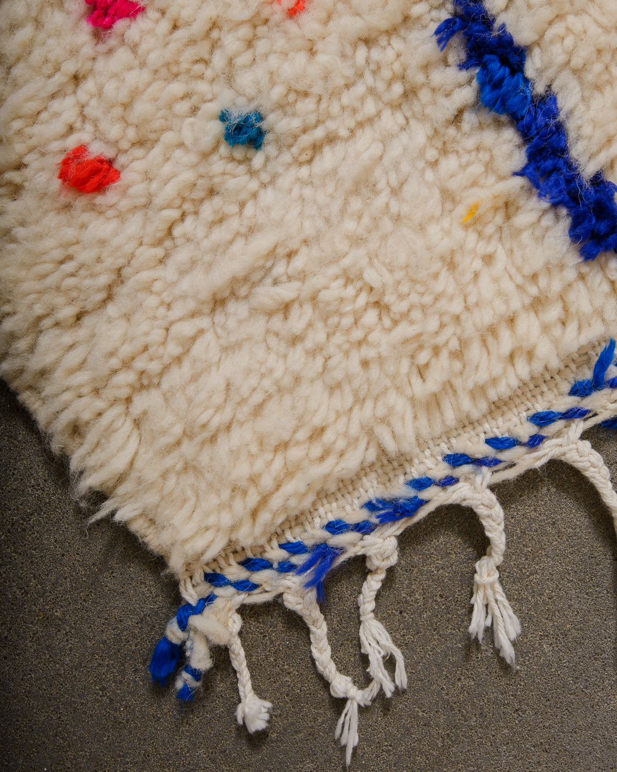 Corner of Azilal rug with cream wool and white cotton tassels and blue and white weaving across the edge.