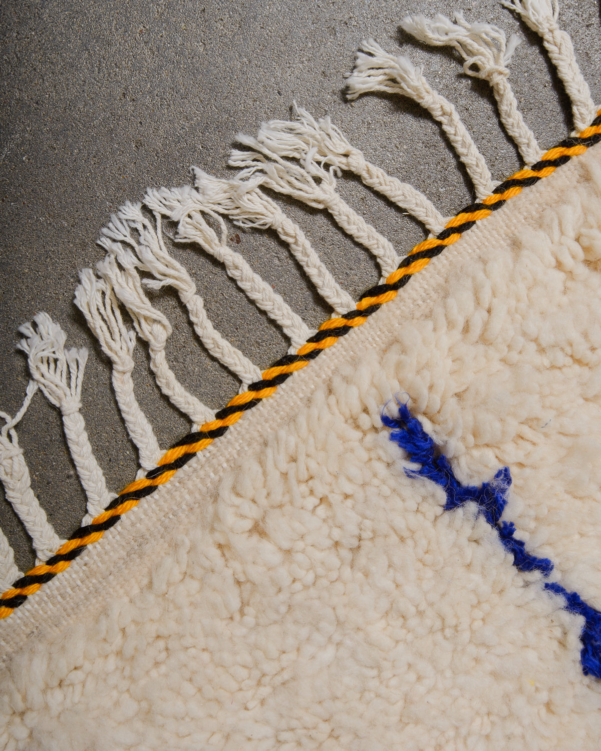 Edge of Azilal rug with white cotton tassels and black and yellow weaving across the edge.