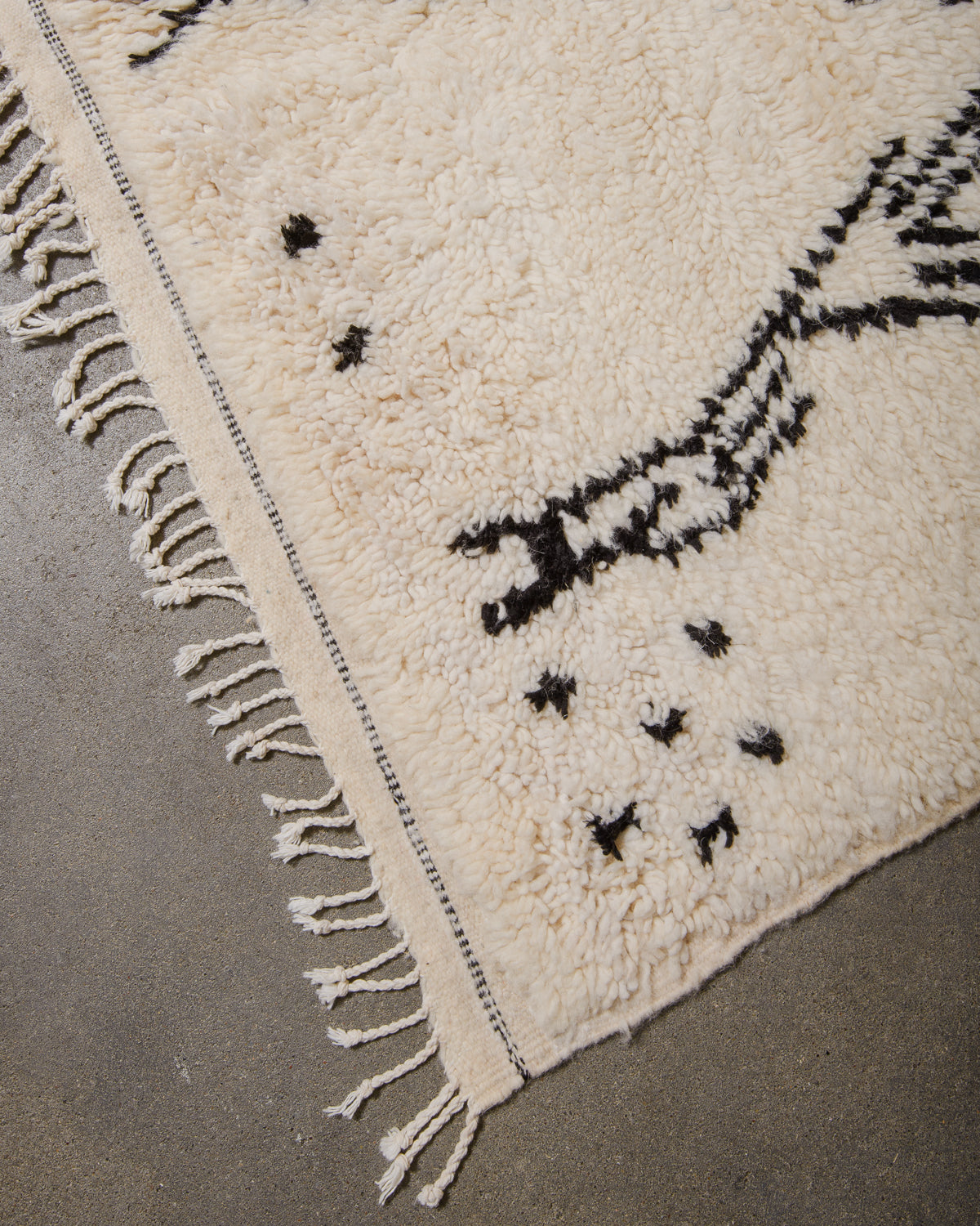 Edge of Azilal rug with white cotton tassels and black and white weaving across the edge.