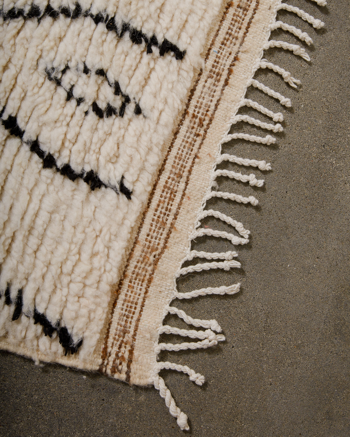 Edge of Azilal rug with white cotton tassels and brown weaving across the end.