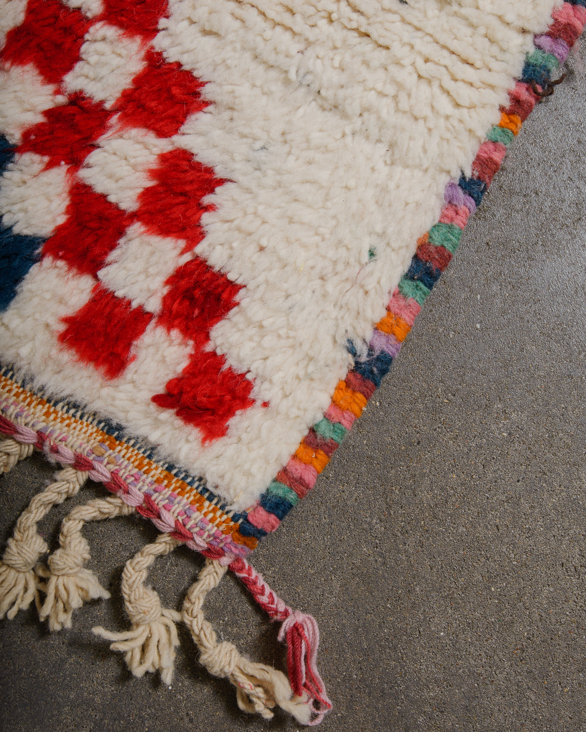 Corner of wool berber rug that is finished with tightly woven colourful wool edges and natural wool tassels across the ends.