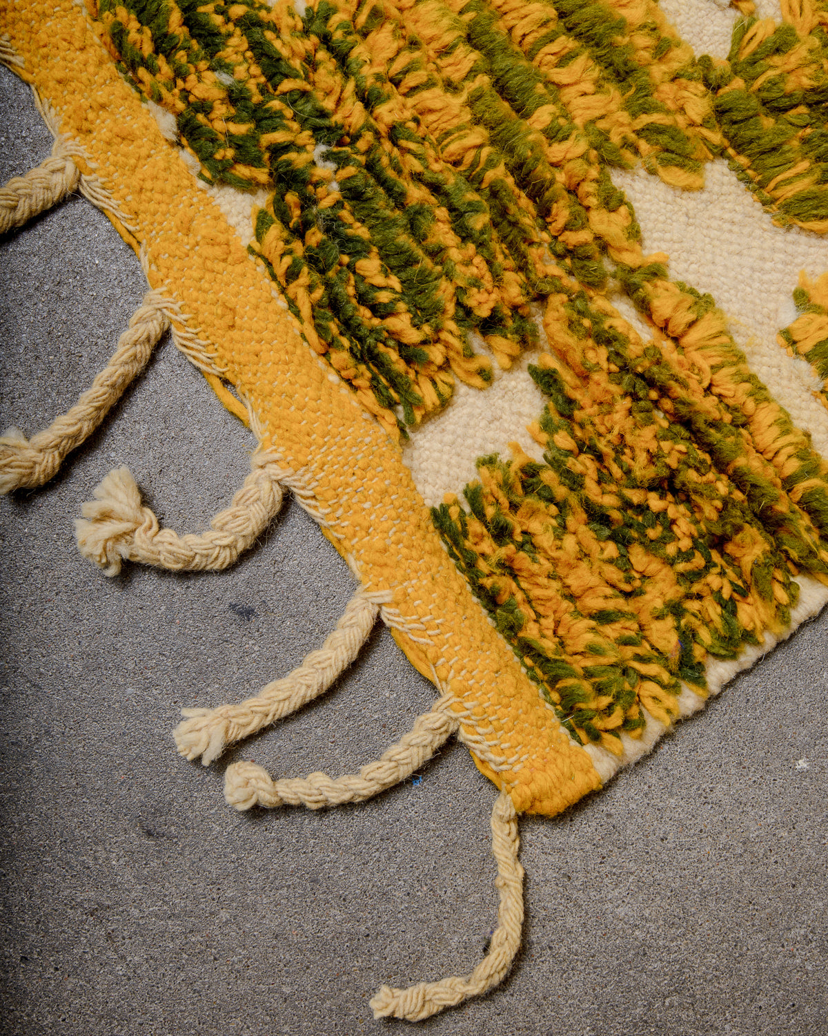 Corner of Berber runner rug with a yellow woven edge and natural wool tassels. 