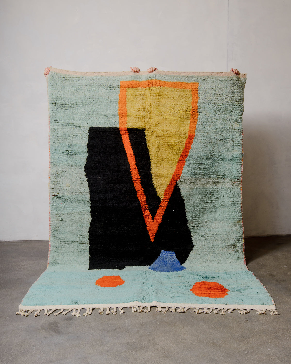 Berberlin vintage Berber rug made of colourful wool being held up by four hands in front of a white wall. 