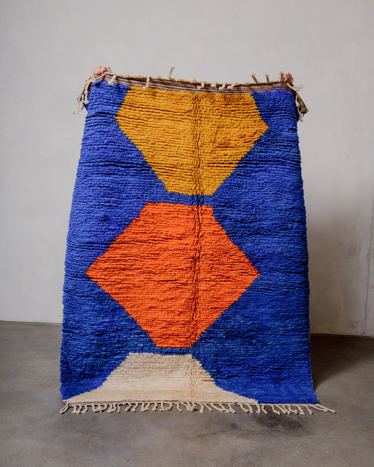 Berberlin vintage wool boujad rug in bold colours being held up in front of a white wall. 