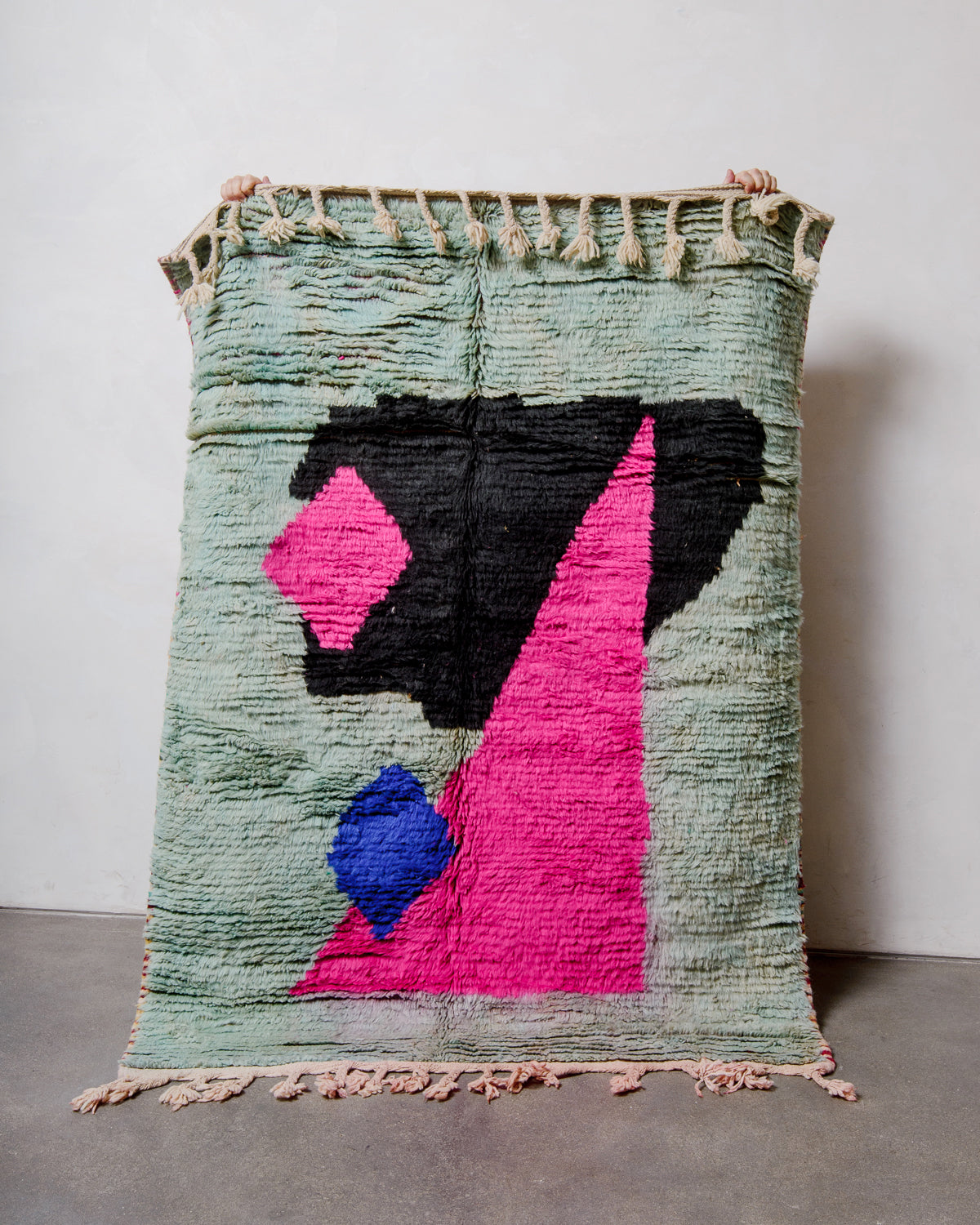 Berberlin vintage boujad rug in colourful wool being held up in front of a white wall.