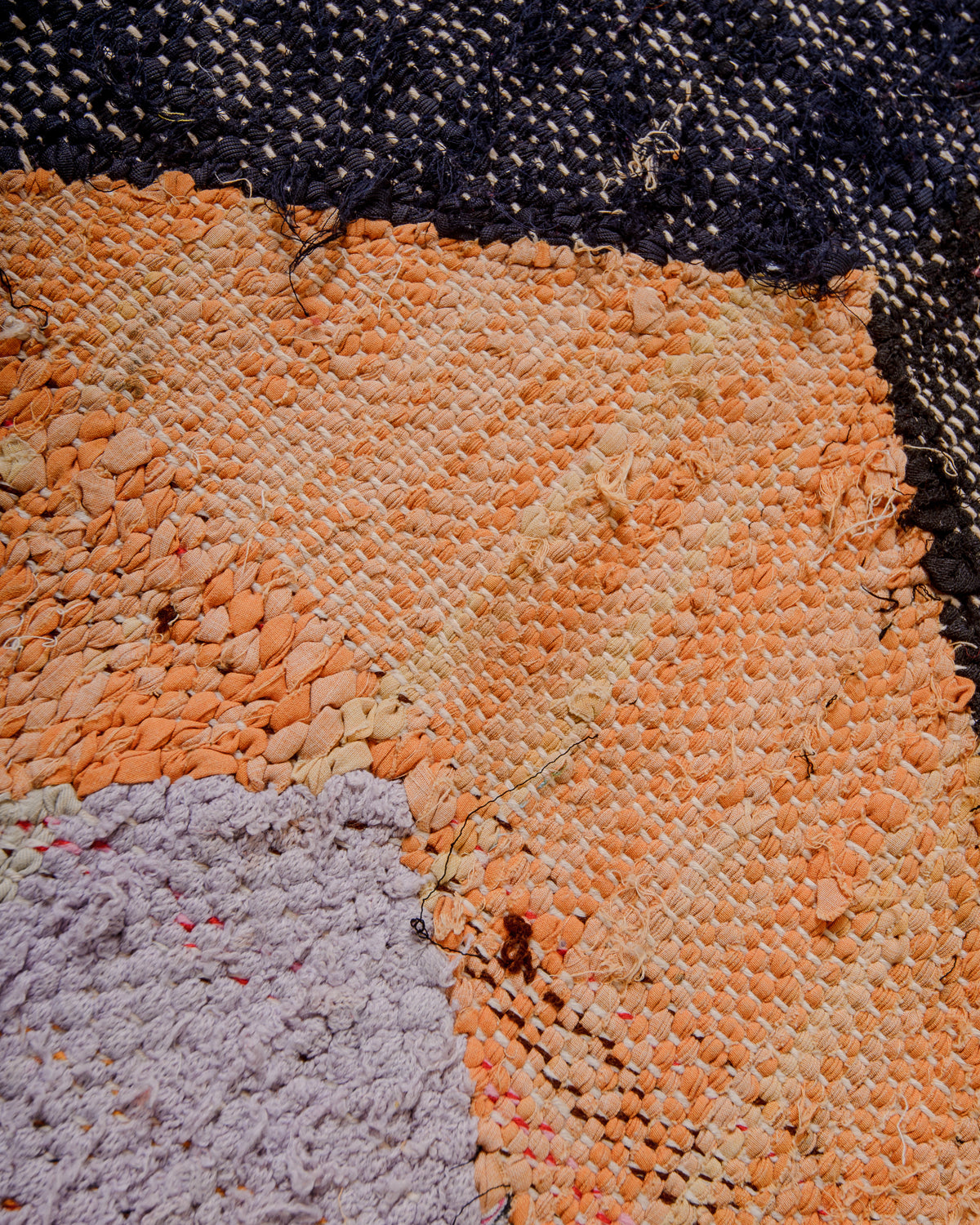 Different textures on the surface of a Berber Kelim rug in orange, black and lavender.