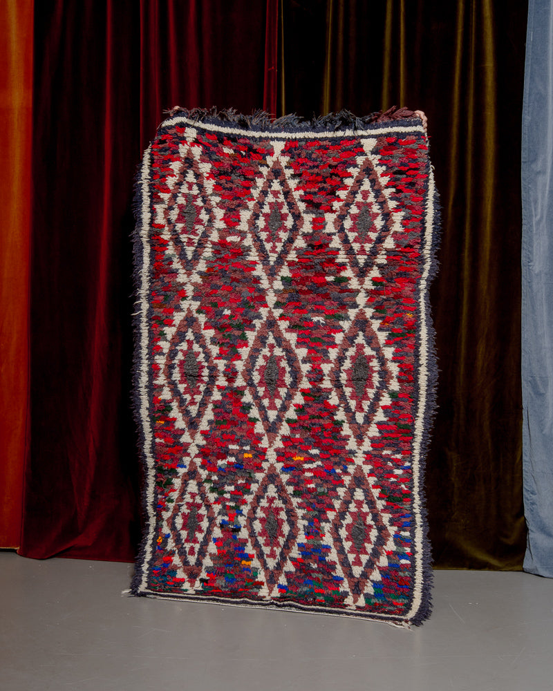 Berberlin Vintage boucherouite runner rug being held up in front of a velvet curtains. 