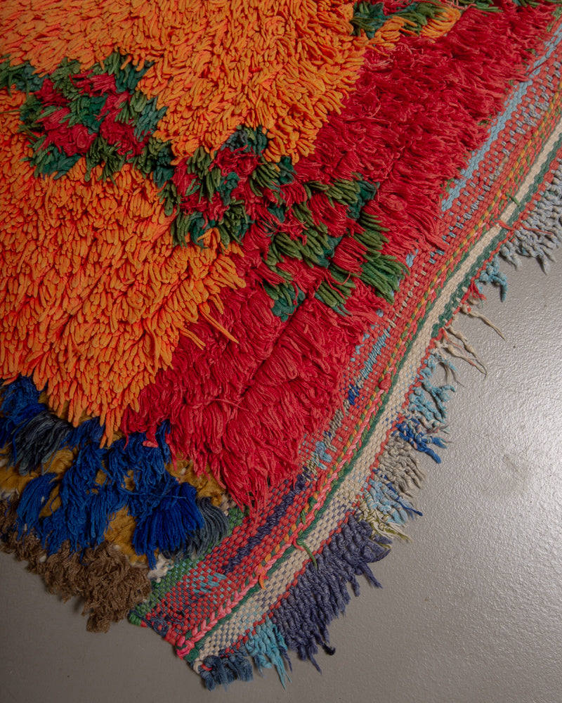 Corner of boucherouite rug with red, blue green and orange and colourful woven end with tassels.