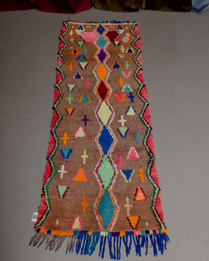 Vintage Berberlin boucherouite runner rug on grey floor in front of velvet curtain. 