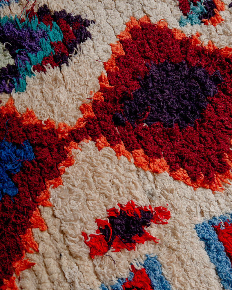 Surface of boucherouite rug with red, blue, orange, purple and burgundy cotton  cream wool.