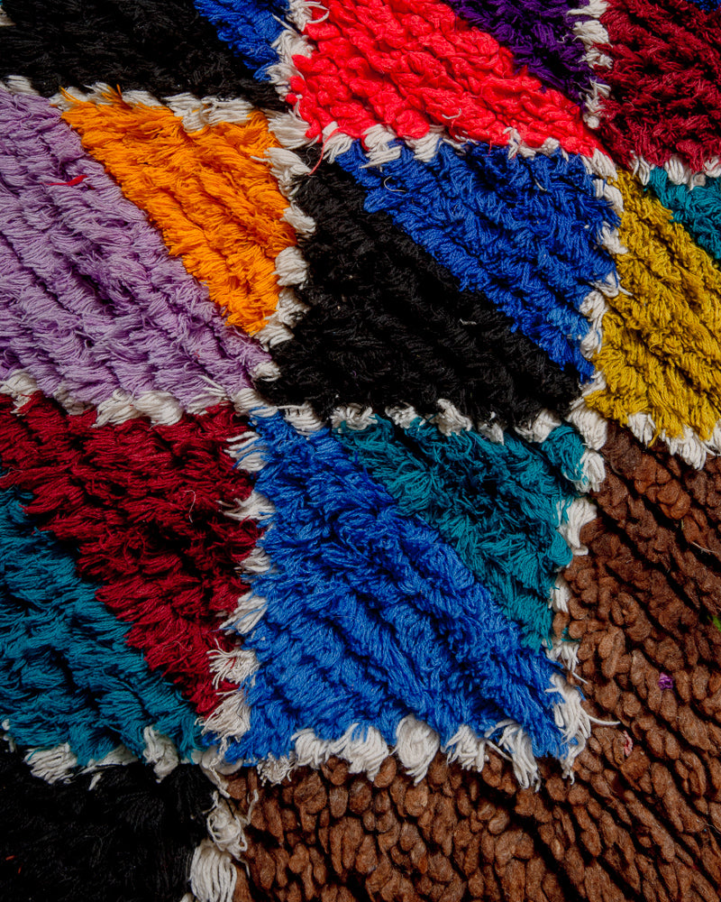 Surface of boucherouite rug with red, blue mustard and purple yarn and brown wool.