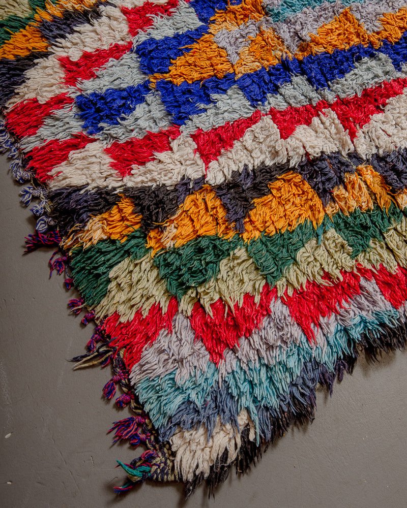 Corner of boucherouite rug with red, blue green and white yarn and short tassels.
