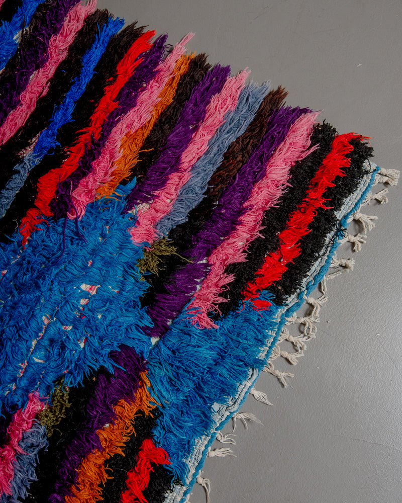 Corner of boucherouite rug with colourful cotton striped pattern and short cotton tassels.