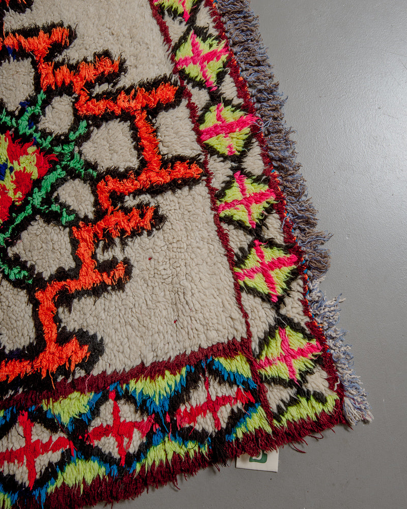Corner of boucherouite rug with orange, green, burgundy and black cotton and cream wool.